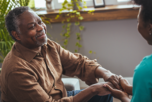 An individual sitting indoors holds the hands of another individual who is seated across from the